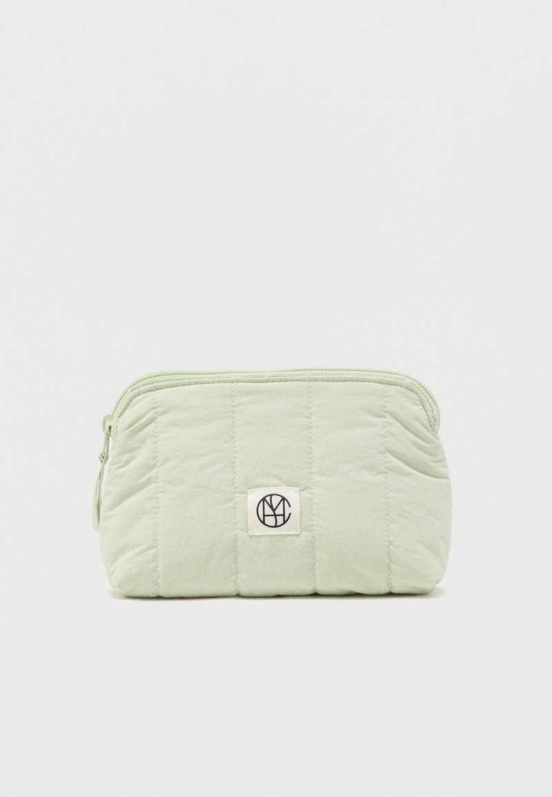 Φωτεινή πράσινη τσαντάκι από καπιτονέ ύφασμα με κλείσιμο με φερμουάρ και μικρό τετράγωνο διακριτικό λογότυπο στο κέντρο μπροστά.