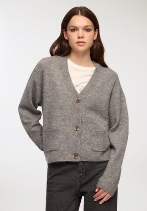 Cardigan grigio lavorato a maglia con scollo a V, bottoni in legno e due tasche frontali. Presenta polsini e orlo a coste per texture e forma.