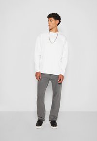 Camisa blanca de manga larga combinada con jeans grises de pierna recta. Zapatillas negras con suelas blancas y un collar de cadena plateado como detalle destacado.
