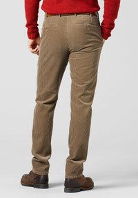 Bruine corduroy broek met een slanke pasvorm, met verticale ribbels, twee achterzakken en een riemlusdetail. Gecombineerd met donkere schoenen.