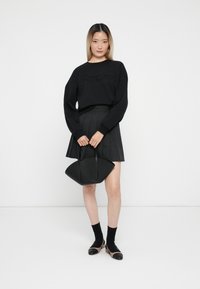 Felpa nera con la scritta "Amore" in borchie, gonna nera plissettata, borsa nera a forma di ventaglio e calze nere con scarpe con tacco.