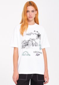 Witte katoenen t-shirt met een oversized pasvorm, voorzien van grafische illustraties in zwart en groen. Opvallende details zijn de merknaam "VOLCOM" in een schreeflettertype.