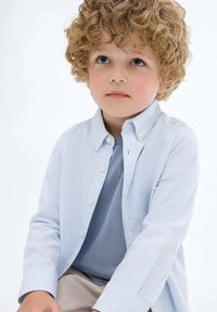 Sininen ja valkoinen raidallinen nappipaita, joka on kerrottu vaalean sinisen t-paidan päälle, lapsella, jolla on karhea, kihara vaalea hius.