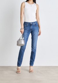 Ljusblå jeans med smal passform, i kombination med en vit ribbad linne, beiga klacksandaler och en silvrig handväska med kedjedetalj.