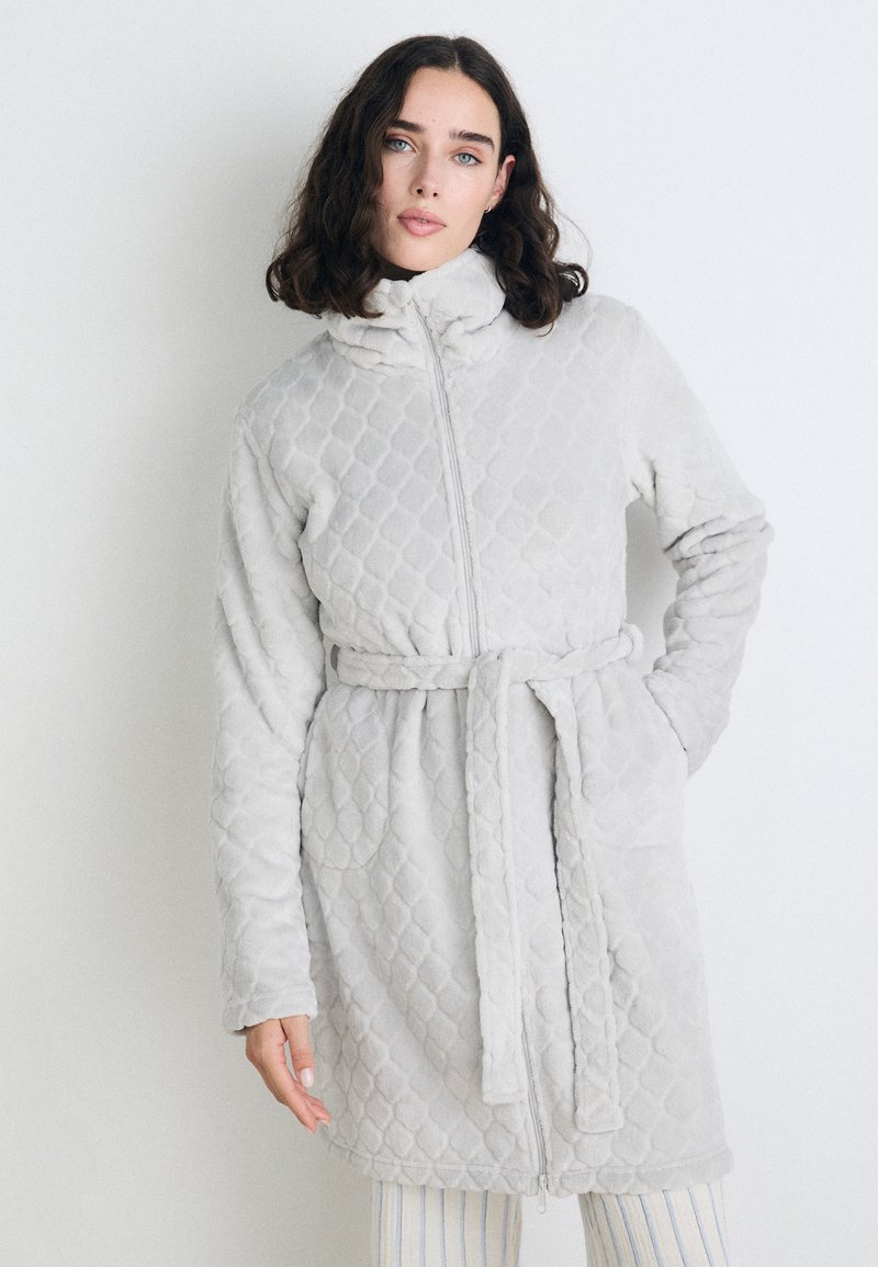 Rochie de dormit căptușită de culoare gri deschis, cu guler înalt, fermoar complet, cordon și buzunare laterale. Textură moale cu un model în diamant pe toată suprafața.