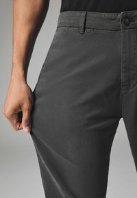 Dunkelgraue Chinos mit glatter Textur, geradem Schnitt, Fronttaschen und einem Knopfverschluss am Bund.