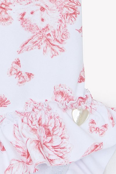 Λευκό ύφασμα διακοσμημένο με ροζ λουλουδάτα και πεταλούδα σχέδια, με βολάν στο τελείωμα και ασημένιο διακοσμητικό σε σχήμα καρδιάς.