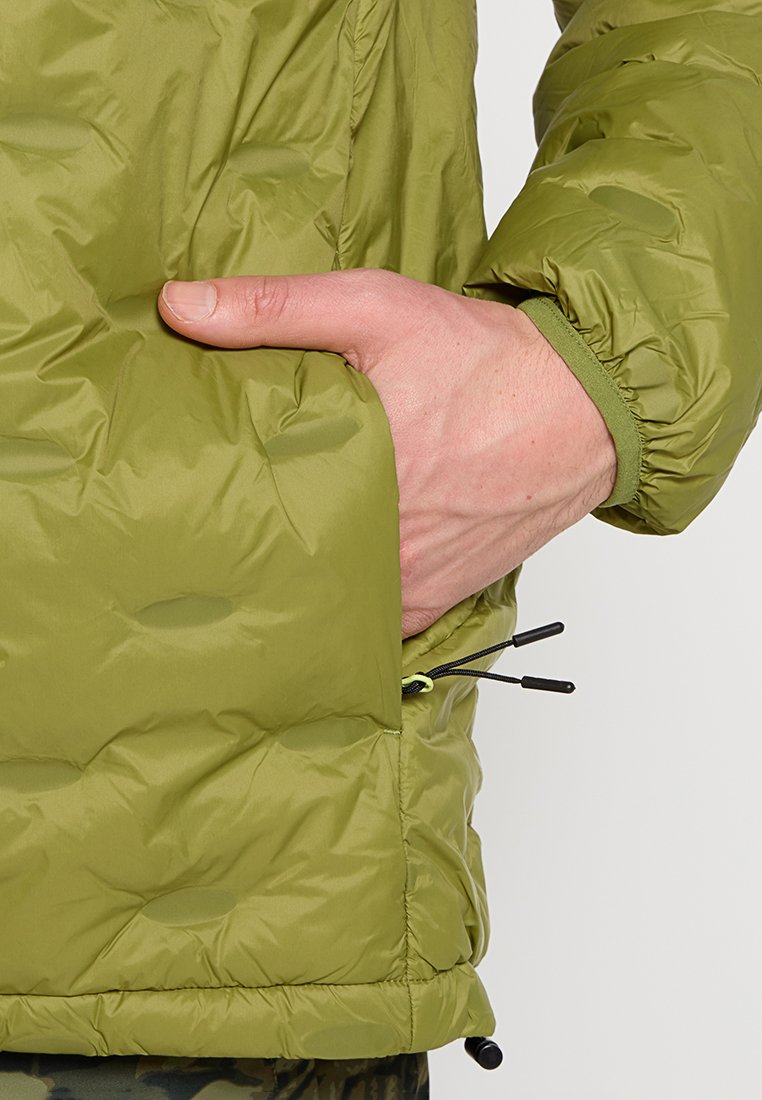 Chaqueta acolchada verde oliva con un diseño texturizado y acolchado. Presenta un bolsillo lateral y toggle ajustables en el bajo para un ajuste personalizado.