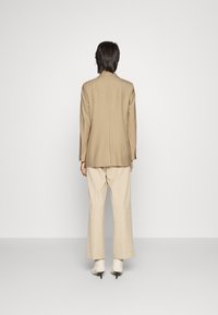 Blazer beige entallado de corte recto, combinado con pantalones de pierna ancha de un beige claro. El modelo lleva botas de tobillo blancas con textura.