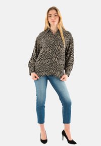 Camicia oversize a righe zebra nera e crema, con bottone davanti, in tessuto morbido, abbinata a jeans blu fitted e tacchi alti neri.