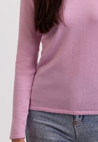 Ljusrosa långärmad tröja med rund halsringning, tillverkad av mjukt, texturerat tyg, i kombination med ljusblå denimjeans.