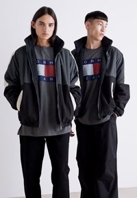 Dos modelos luciendo chaquetas contrastantes y camisetas gráficas. Las chaquetas son oscuras con acentos claros; las camisetas son grises con un logotipo audaz.