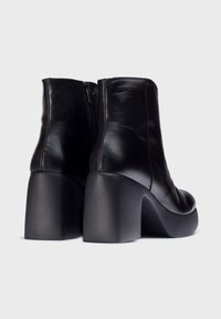 Botines de cuero negro hasta el tobillo con punta redonda, tacón alto y cuadrado, y un acabado suave. Con cremallera trasera para el cierre.