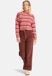 Maglione a righe rosse lavorato a maglia con design cropped, abbinato a pantaloni in corduroy marroni a gamba larga e scarpe da ginnastica chiare. Completo casual.