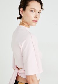 Rosa cropped topp laget av mykt stoff, med korte ermer og et knytedetalj på baksiden. Glatt tekstur og avslappet passform.