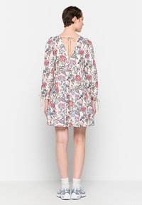 Blumenmuster-Kleid mit langen Puffärmeln, V-Ausschnitt und Bindeschluss. Der beigefarbene Stoff hat pinke und blaue Muster. Ausgestellter Rock in Midi-Länge bis zur Oberschenkelmitte.