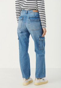 Los pantalones cargo de denim de color azul claro presentan un diseño de pierna recta, múltiples bolsillos y un parche de logo visible en la cinturilla.