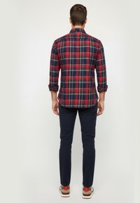 Camisa de cuadros rojos y azul marino con mangas largas, cuello abotonado y puños enrollados, combinada con pantalones azul marino y zapatillas marrones.