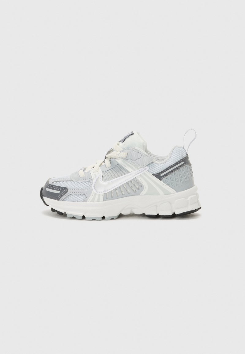 Lahka športna obutev z zgornjim delom iz sive in bele mrežaste tkanine, ki ima vzorčasto peto, debel podplat in kontrastne črne detajle.