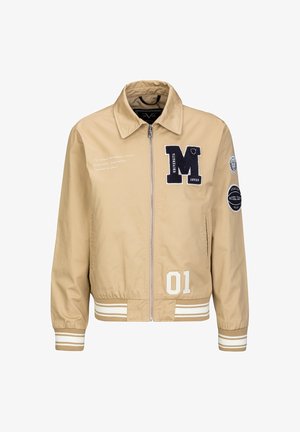 Beige Collegejacke mit Reißverschluss, weißen gestreiften Bündchen und Saum, schwarzem "M"-Aufnäher, der Zahl "01" sowie weiteren Aufnähern und Texten auf Vorderseite und Ärmel.