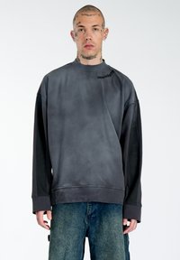 Schwarzes, übergroßes Sweatshirt mit Farbverlauf, rundem Ausschnitt, langen Ärmeln und gesticktem "Multiply"-Text auf der Schulter. Weiche Textur.