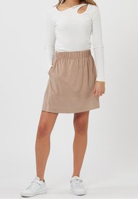 Jupe en daim beige avec taille élastique, longueur genou. Associée à un haut blanc à manches longues avec un décolleté découpé. Baskets blanches.