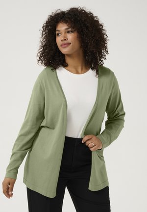 Cardigan verde chiaro, a maniche lunghe, con apertura frontale, realizzato in materiale morbido, abbinato a una camicia bianca e pantaloni neri.
