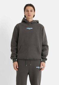 Sudadera gris oscuro con un bolsillo frontal, que presenta un logo azul "SIXTH JUNE PARIS". Tejido cómodo con un corte relajado y capucha ajustable con cordón.