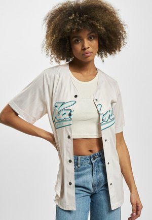 Kurzärmliges Baseball-Jersey in Creme mit türkisfarbenem Schriftzug und vertikalen Streifen. Verfügt über schwarze Knöpfe und einen lässigen Schnitt, getragen über einem Crop-Top.