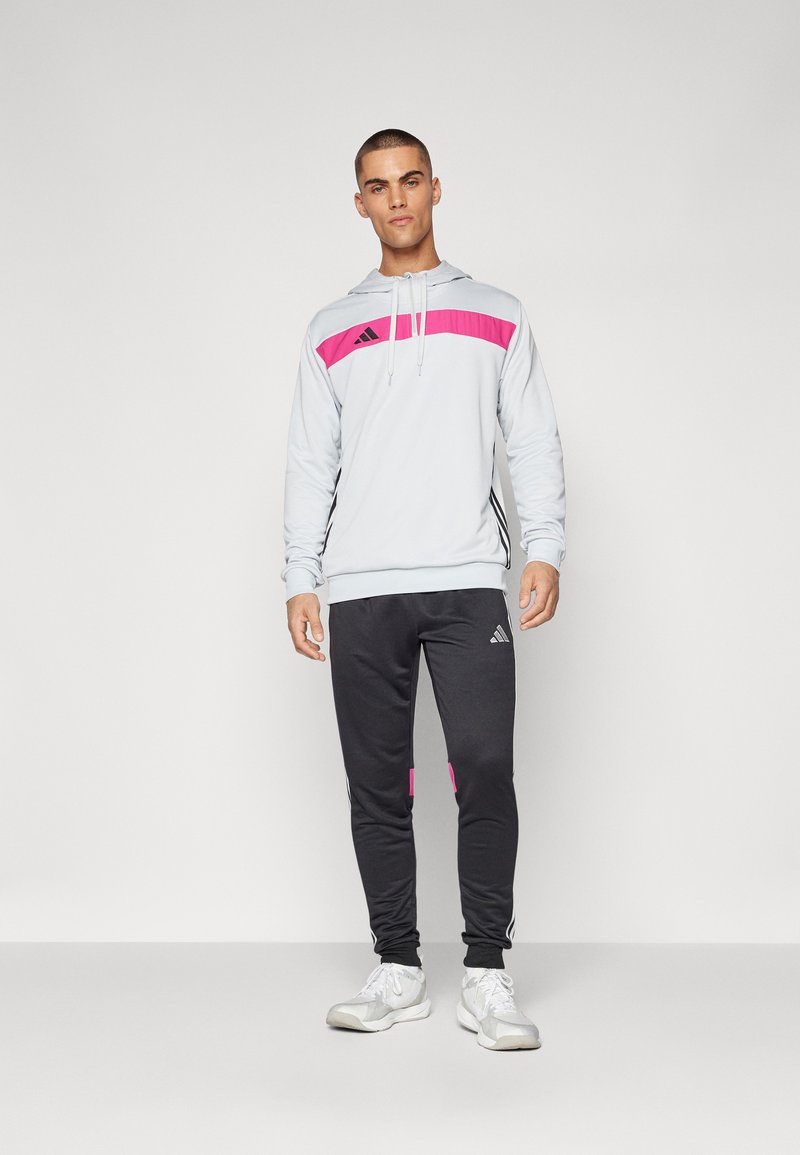 Sudadera con capucha gris y detalles en rosa, logo negro; combinada con pantalones negros que tienen detalles en rosa y franjas blancas. Incluye calzado atlético.