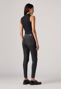 Top senza maniche nera abbinato a jeans skinny grigio scuro a vita alta. Tessuto liscio, dettagli minimi e tasche posteriori discreti. Scarpe nere.
