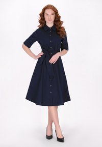 Rochie albastru închis, cu buton și mâneci scurte, talie strânsă cu curea și fustă evazată. Material neted, cu o culoare uniformă și fără modele vizibile.