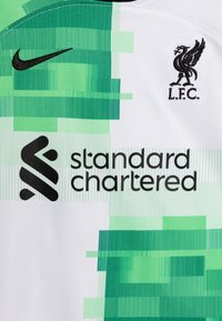 Camiseta de fútbol blanca con un patrón pixelado verde, logo de Nike en negro, y "Standard Chartered" en texto negrita negro, con el emblema de L.F.C.