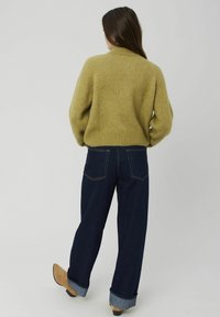 Pull en maille vert olive avec un col haut et un ourlet côtelé, assorti à un jean large bleu foncé, retroussé aux chevilles.