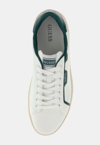 Sneaker bianca con accenti verdi, tomaia in tessuto e sintetico, punta tonda, suola testurizzata, sei occhielli con lacci bianchi e logo "GUESS" sulla linguetta.