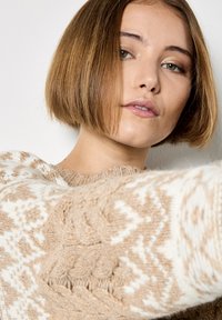 Sweter dzianinowy w beżowym i białym kolorze z misternymi wzorami; posiada teksturowane rękawy i okrągły dekolt. Wykonany z miękkiej mieszanki wełny.