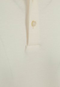 Crème-kleurig poloshirt met een zachte, geribbelde textuur, korte kraag en een enkele parelknopsluiting.