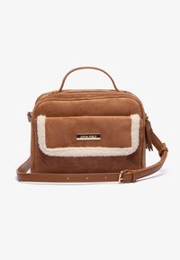 Sac en fausse suède marron avec un rabat en peluche de couleur crème, une poignée supérieure et une sangle ajustable. Présente une plaque logo dorée à l'avant.