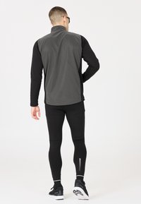 Svart långärmad tröja och åtsittande svarta leggings. Tröjan har ett grått västöverdrag. Leggingsen har ett vertikalt randigt mönster på vaden.