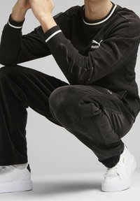 Chándal de terciopelo negro con acentos de rayas blancas, que incluye una parte superior de cuello redondo y pantalones ajustados. Incluye zapatillas blancas.