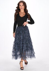 Fekete, hosszú ujjú felső, amelyet egy réteges, kék leopárdmintás tüllszoknyával párosítanak, szűk derékkal és sima fekete magassarkú szandállal.