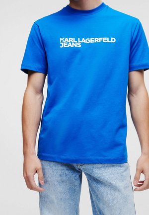 Osoba nosząca jasnoniebieską koszulkę z białym tekstem "KARL LAGERFELD JEANS", w połączeniu z jasnoniebieskimi dżinsami.