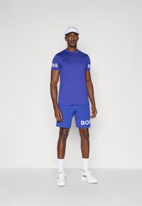 Conjunto atlético azul vibrante composto por uma t-shirt de mangas curtas e calções. Ambas as peças têm a marca "BORG" em branco nas mangas e nos calções.