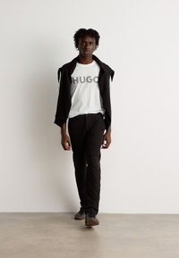 Black jacket over a white T-shirt with "HUGO" logo, paired with black pants and brown shoes. Smooth fabric with a casual fit.