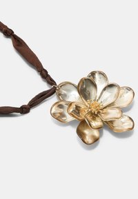 Collana a pendente floreale in oro con forme di petali trasparenti, cordino in tessuto marrone texturizzato e dettagli accurati al centro.