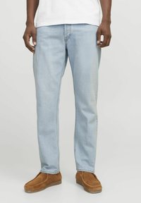 Jeans de mezclilla azul claro con corte recto, que presentan una textura desgastada y diseño de cinco bolsillos, combinados con zapatos de gamuza marrón tipo slip-on.