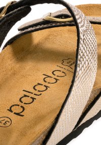 Tan læder flip-flop med metalisk sølv teksturerede stropper, præget af en sort sål og guld hardware. Indeholder branding på indersålen.