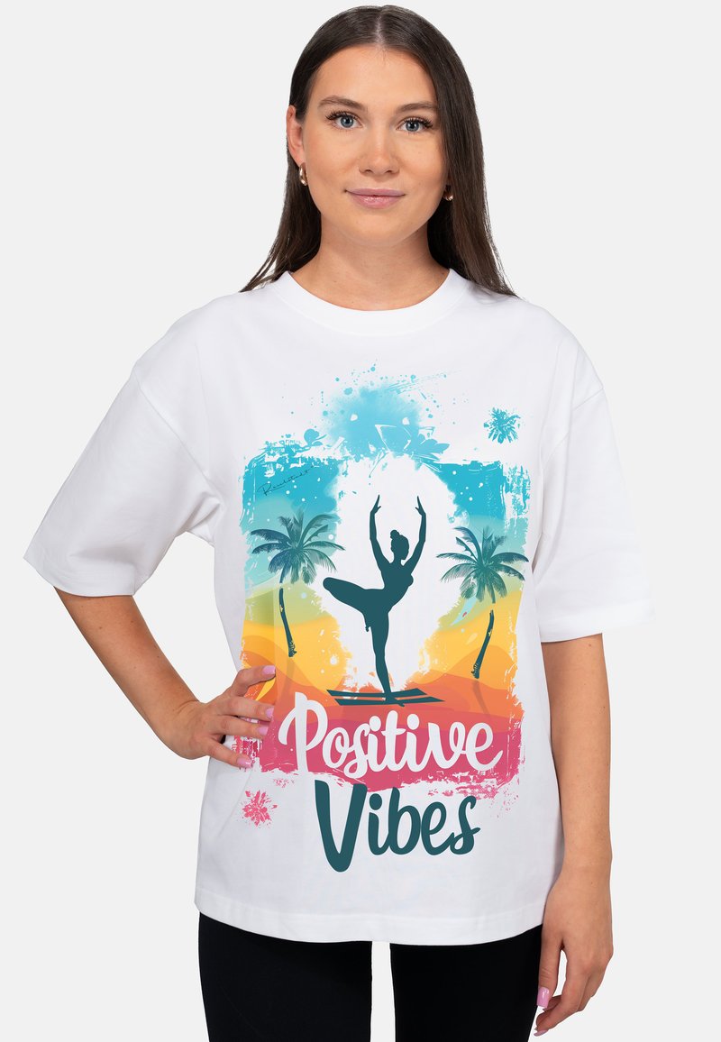 T-shirt blanc oversize avec un motif coloré représentant une danseuse, des palmiers, et le texte « Positive Vibes » en polices ludiques.