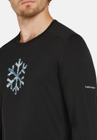 Svart långärmad skjorta i mjukt material, med en flerfärgad snöflinge-grafik på bröstet och "icebreaker"-logotypen på ärmen.