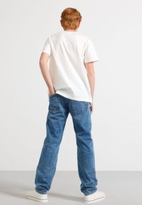 White short-sleeve t-shirt paired with light blue denim jeans. The jeans feature back pockets and a slightly relaxed fit. White sneakers.